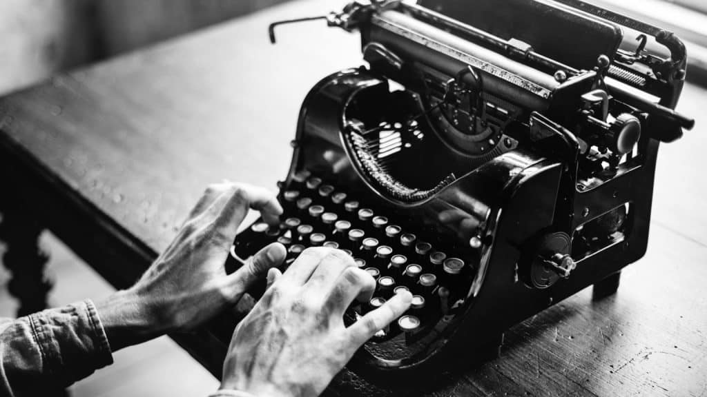 Uma foto em preto e branco de uma pessoa digitando em uma máquina de escrever.